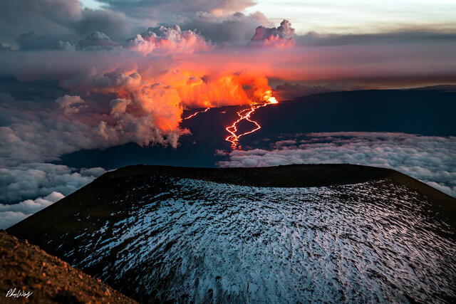 Snow covered Mauna Kea foreground with glowing Mauna Loa lava eruption and clouds on the Big Island.