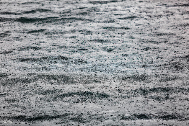 Abstract close up of rain falling on ocean water, creating rippling textures and soft gray patterns in Kona, Hawaii.