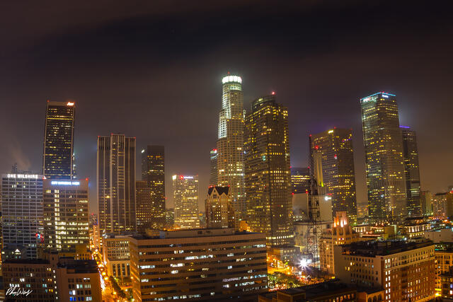 Nighttime city skyline of downtown Los Angeles with illuminated skyscrapers and warm urban lights.