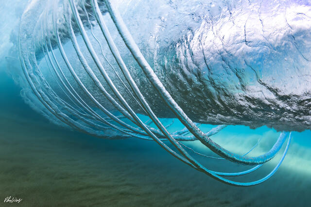 Underwater wave rings and flowing currents beneath a breaking wave in blue ocean water.