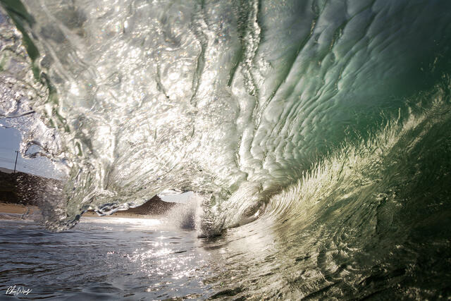 Powerful green ocean wave curling near the shoreline in Malibu, California.
