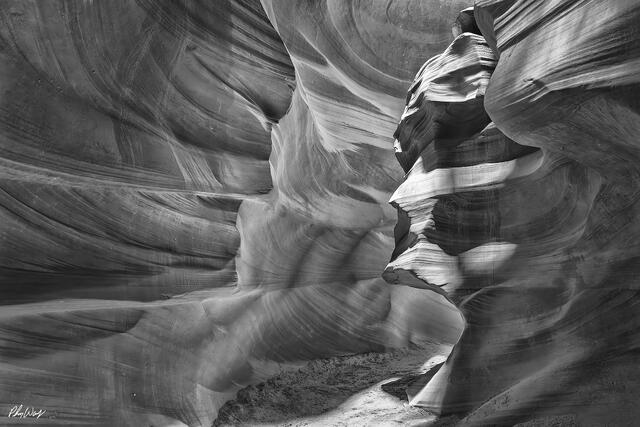 Curved sandstone walls with layered textures and shadows inside a narrow canyon in black and white.