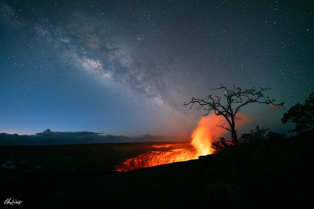 Milky Way above glowing lava crater with silhouetted tree at Volcano National Park on the Big Island of Hawaii.