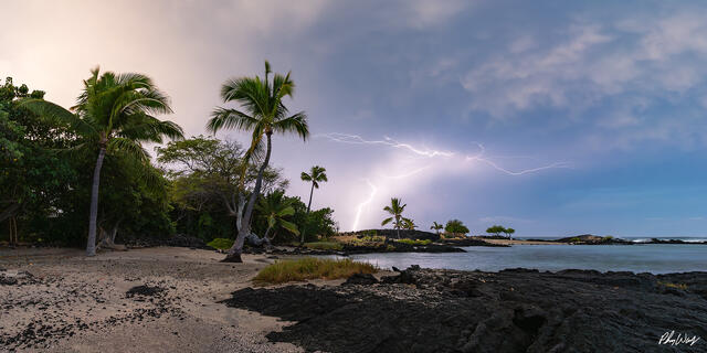 Lightning strike over palm trees and a rocky shoreline in Kona on the Big Island of Hawaii.