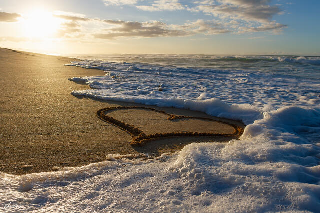 Heart shape drawn in wet sand at Sunset Beach with ocean waves and golden sunset light on Oahu, Hawaii.