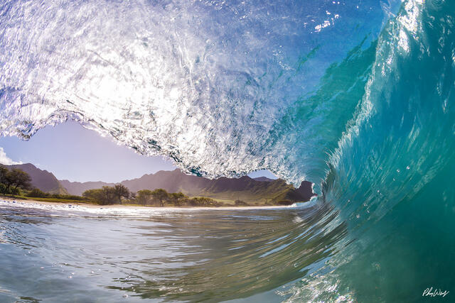 Turquoise ocean wave curling near a tropical beach with mountains in Oahu Hawaii.