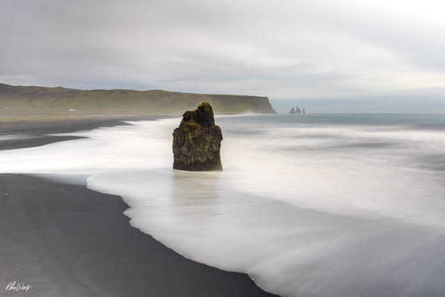 Long exposure ocean waves surrounding a sea stack on Reynisfjara Beach in Iceland.