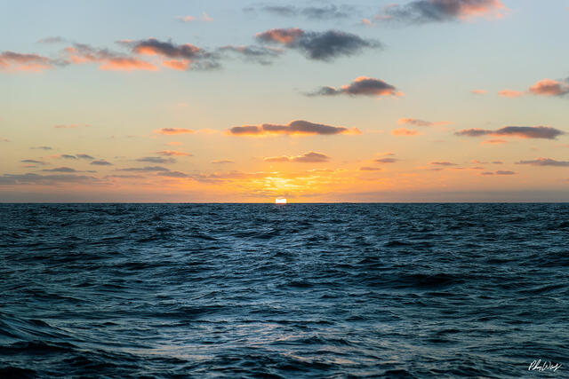 Sun setting on ocean horizon with clouds and calm water near Ensenada Mexico.