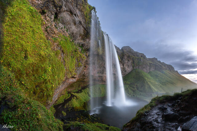 Waterfall flowing from moss covered cliff at Gljúfrabúi Iceland with lush green landscape.