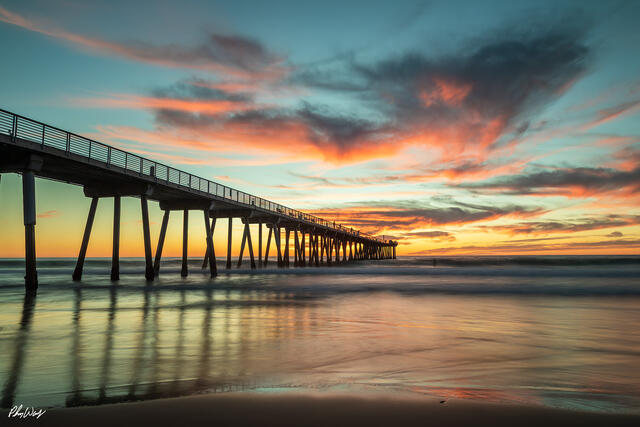 Sunset view of the Manhattan Beach Pier with colorful clouds and smooth ocean reflections in California.