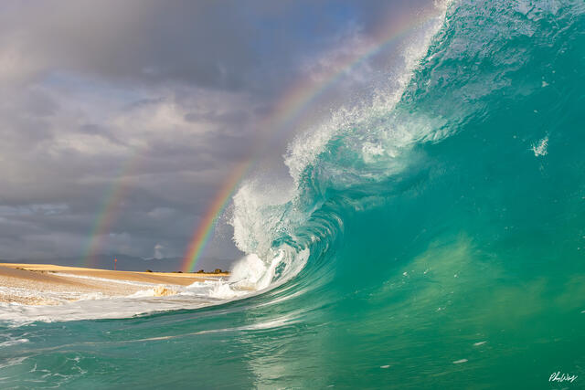 Turquoise ocean wave curling near shore with rainbow on Oahu Hawaii.