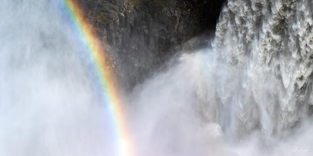 Rainbow cutting through mist beside powerful waterfall at Dettifoss Iceland.