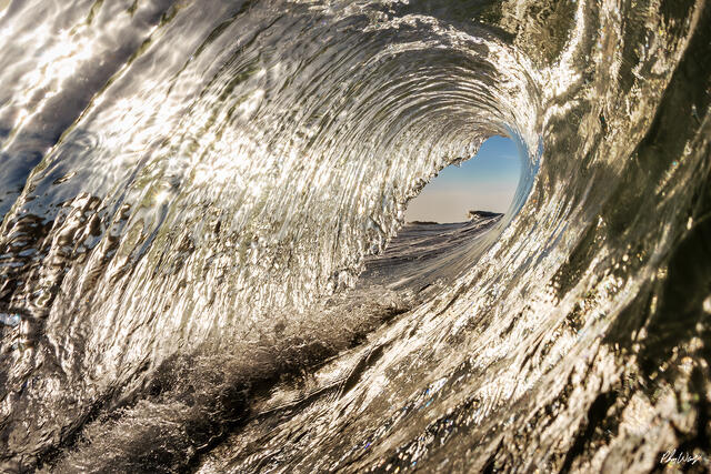 Inside view of a curling ocean wave forming a barrel with sunlight reflecting through the water in Malibu, California.