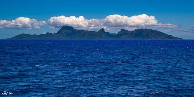 Distant view of Mo'orea Island with volcanic mountains rising above the ocean in Tahiti.