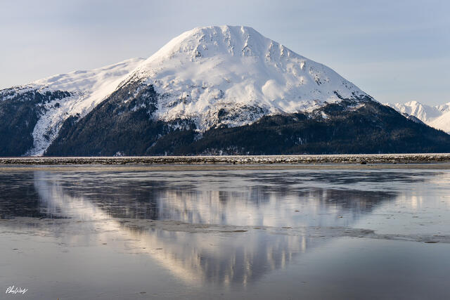 Snow covered mountain reflected in calm icy water under a clear winter sky in Kenai Alaska.