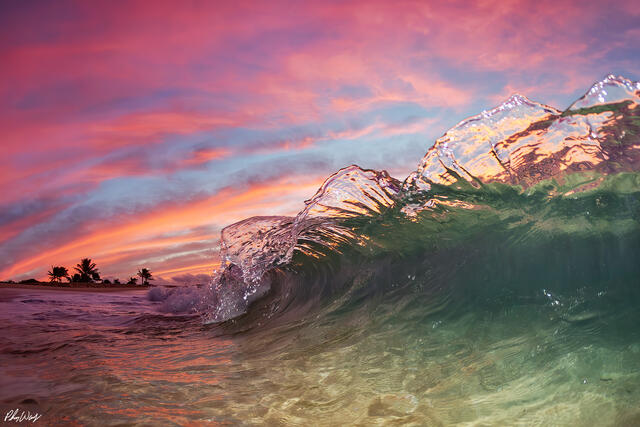 Translucent ocean wave at Sandy Beach Oahu under colorful sunset sky.