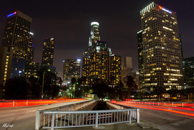 Nighttime photograph of downtown Los Angeles skyline with long exposure red light trails crossing a bridge.