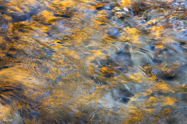 Abstract flowing stream with golden sunlight reflections and blue tones creating a textured water pattern in Kona, Hawaii.
