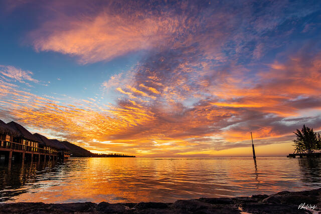 Colorful sunset over calm lagoon water with clouds reflecting in Mo'orea Tahiti.