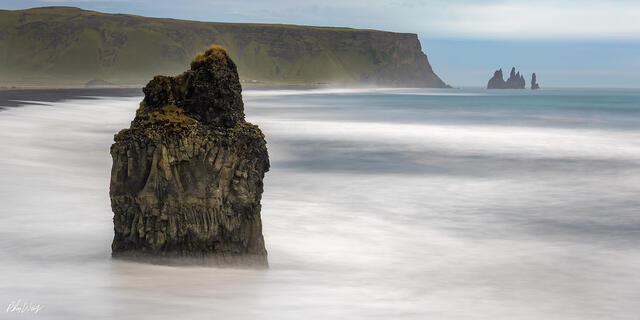 Sea stack rising from smooth ocean water at Reynisfjara Beach Iceland.