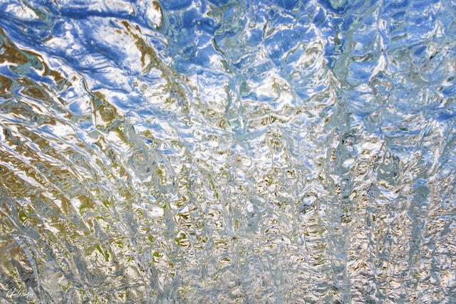 Abstract close up of a breaking wave with rippling water textures, light reflections, and blue tones in Kona, Hawaii.