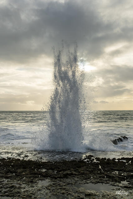 Ocean wave exploding upward into spray against rocky shoreline in Ensenada Mexico.