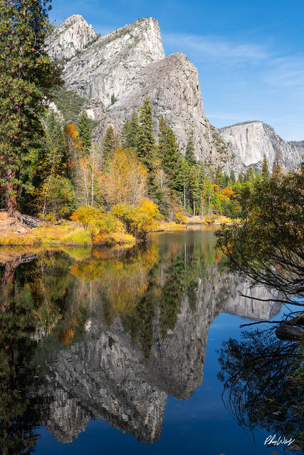 Three Brothers rock formation reflected in the Merced River with autumn trees in Yosemite Valley, California.