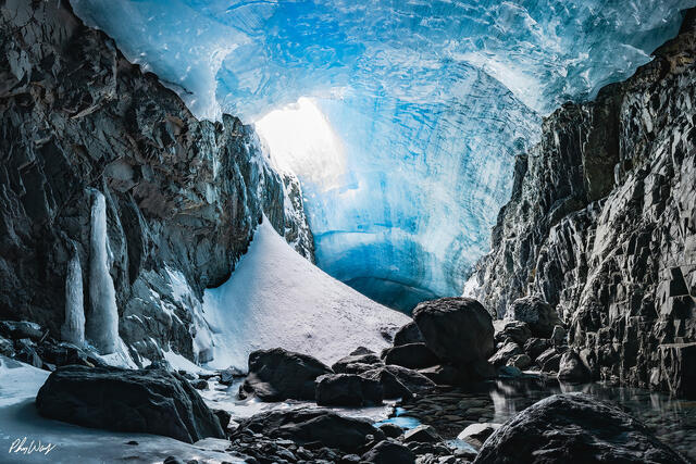 Blue ice cave with snow and rock walls illuminated by natural light in Kenai Alaska.