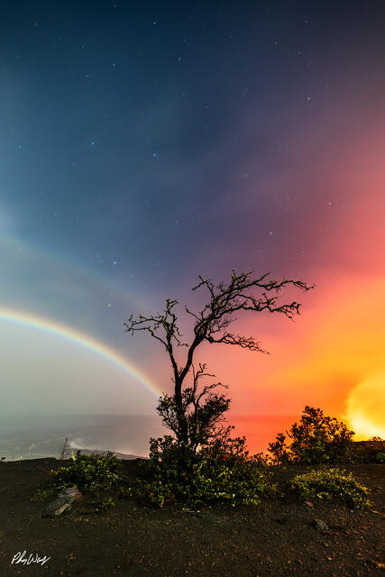 Moonbow arching over glowing lava with silhouetted tree at Volcano National Park on the Big Island of Hawaii.