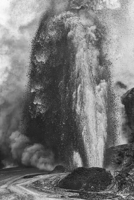 Volcanic eruption sending ash and debris upward with steam clouds and rugged terrain in black and white at Volcano National Park on the Big Island of Hawaii.