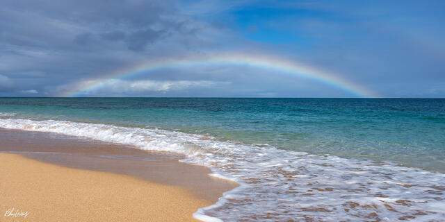 Rainbow arching over ocean waves breaking on sandy beach in Haleiwa, North Shore, Oahu, Hawaii.