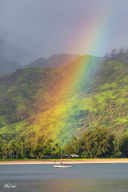 Bright rainbow over lush green mountains and calm waters at Hanalei Bay on Kauai, Hawaii.