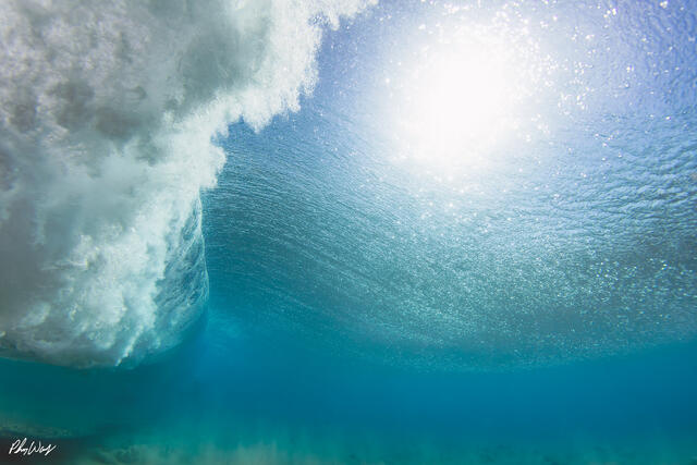 Underwater view of a powerful ocean wave rising toward the surface with sunlight filtering through clear blue water in Haleiwa, Oahu.