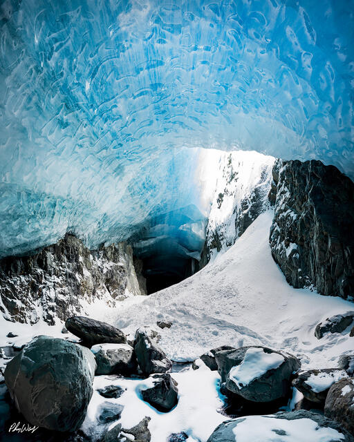 Blue glacier ice cave opening with snow covered rocks and light filtering through in Kenai Alaska.