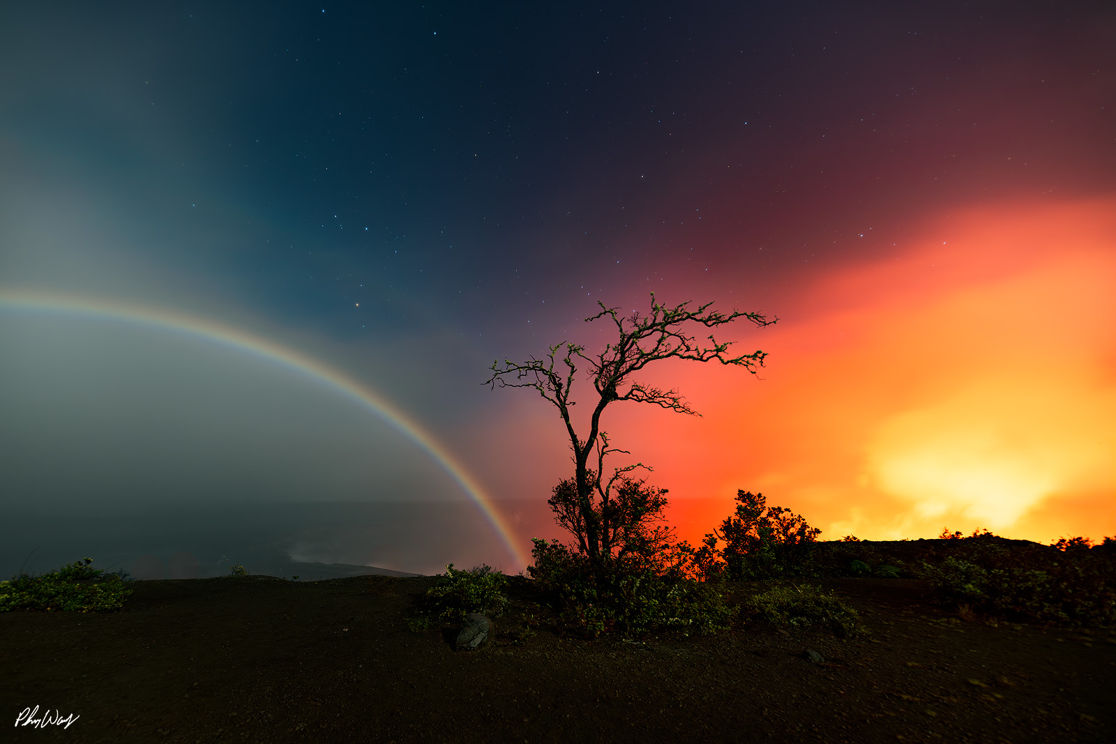 Moonbow Lava Combination Moonbow arching across the night sky with glowing lava light and a silhouetted tree in Volcanoes National Park Hawaii.