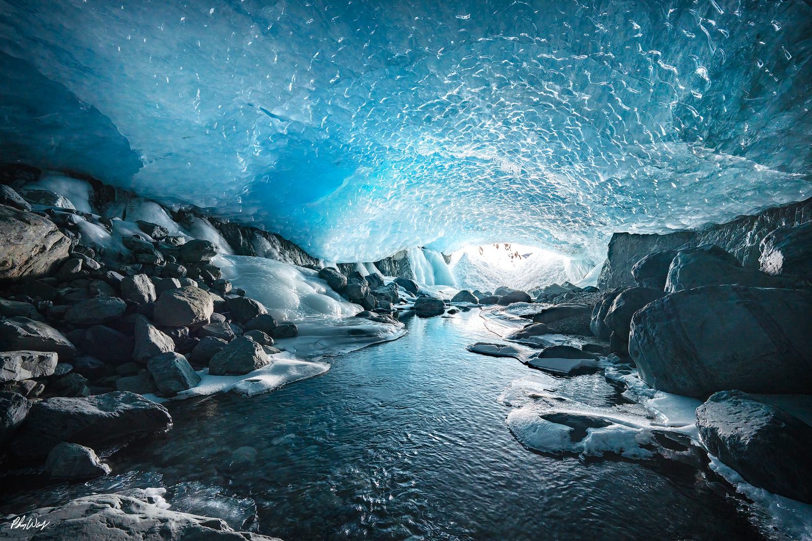 Ice River Clear river flowing through a blue ice cave with rocks and frozen walls in Kenai Alaska.