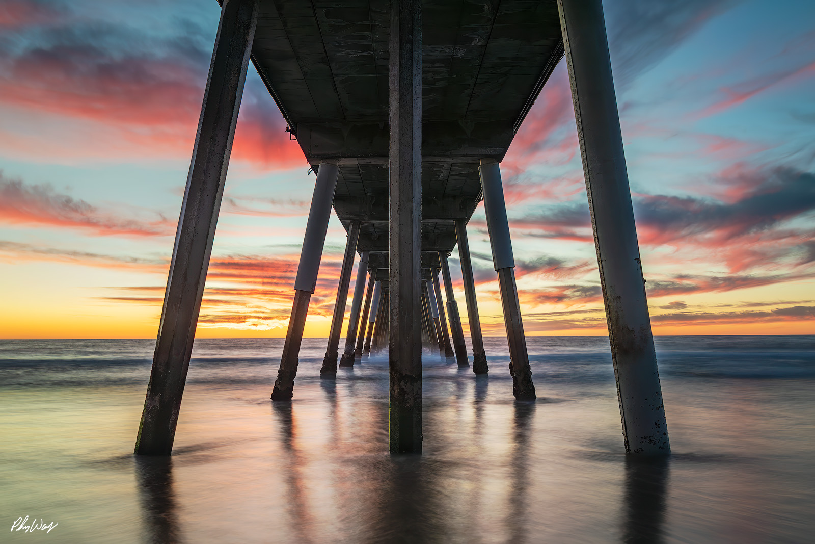 Manhattan Sunset Pier Sunset viewed from beneath the Manhattan Beach Pier with colorful clouds and smooth ocean water in California.