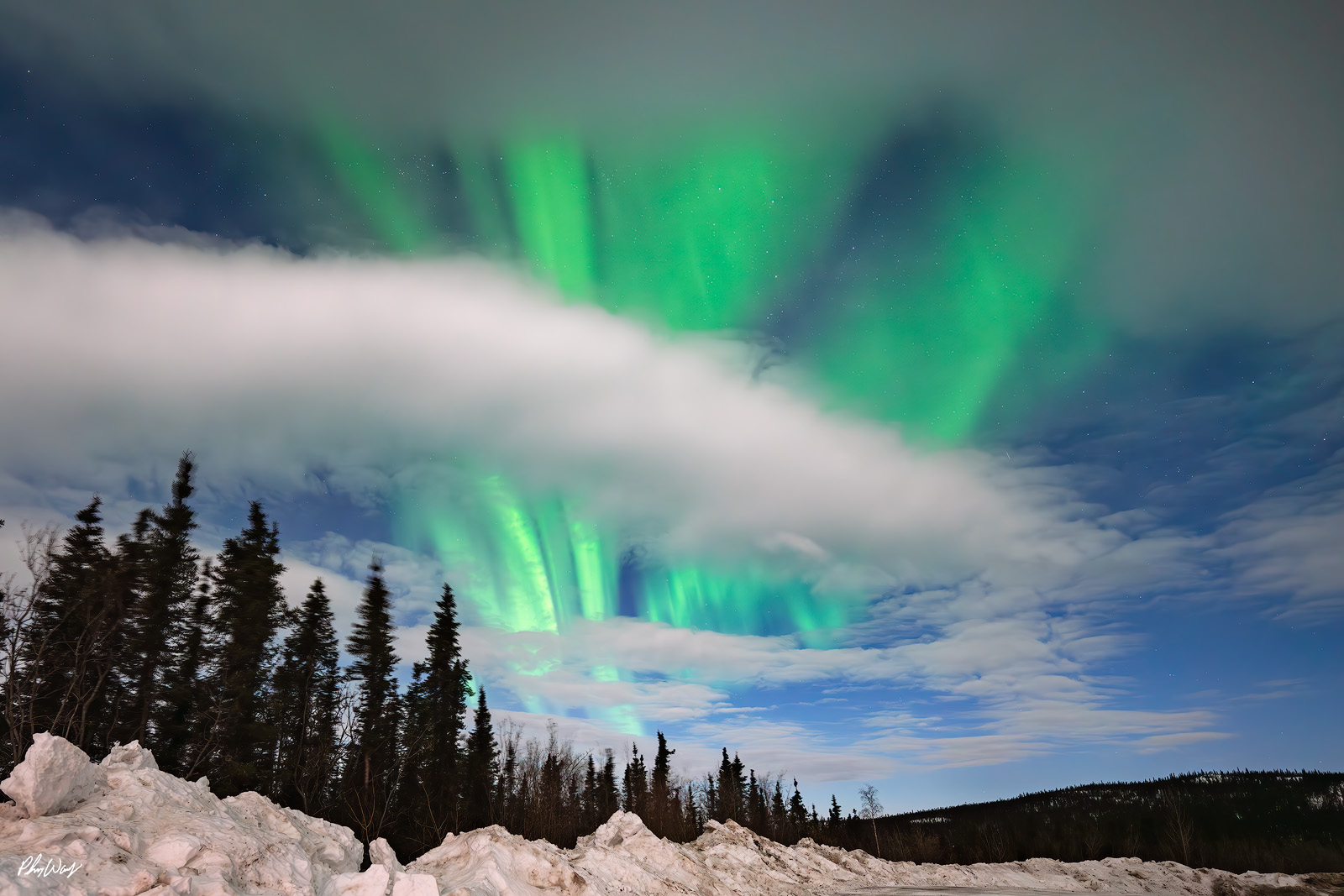 Aurora Moon Clouds Green northern lights glowing through low clouds above snow covered ground and trees in the White Mountains Yukon Alaska.