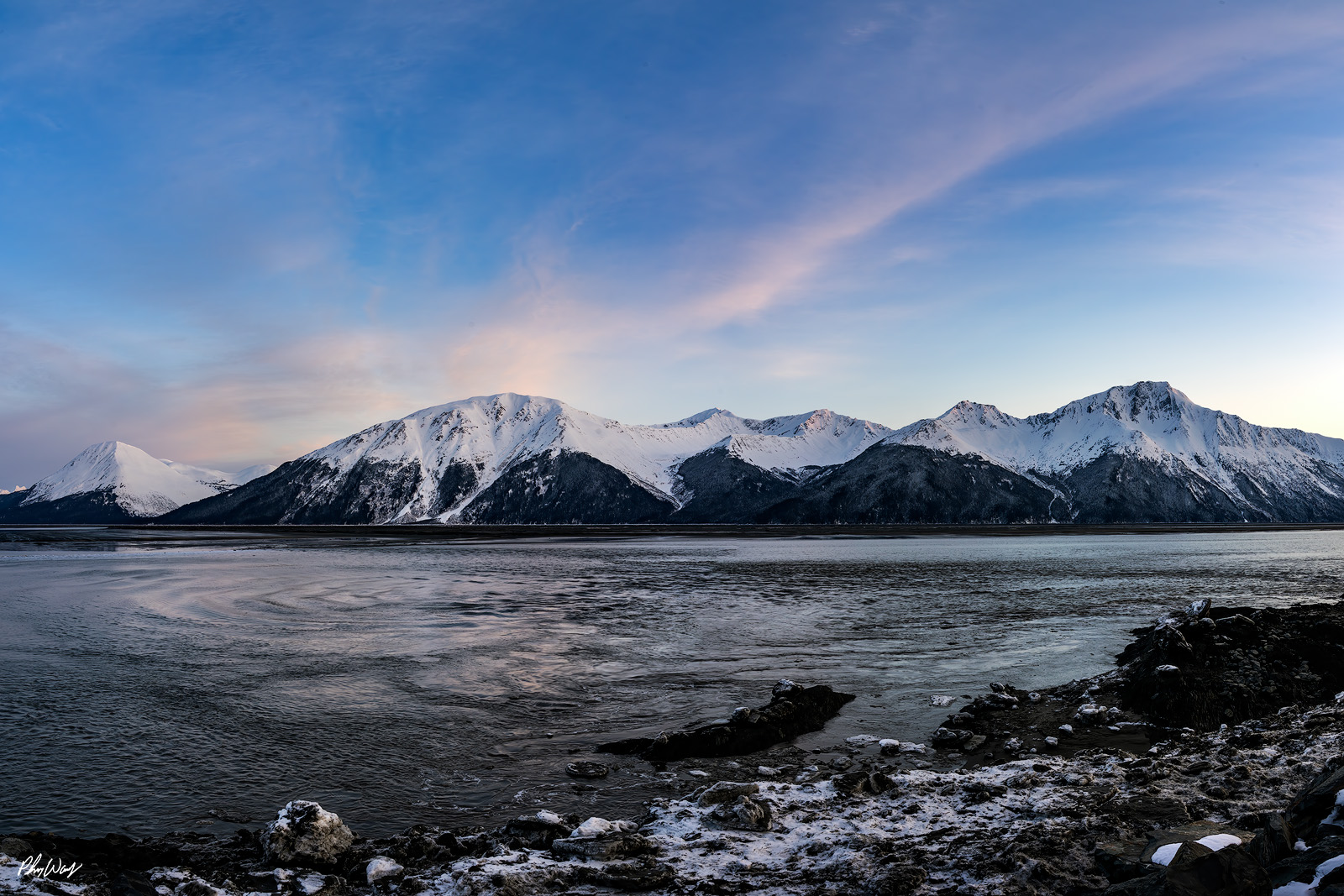 Dreamy Anchorage Snow covered mountains above calm tidal water beneath a pastel sky in Kenai Alaska.