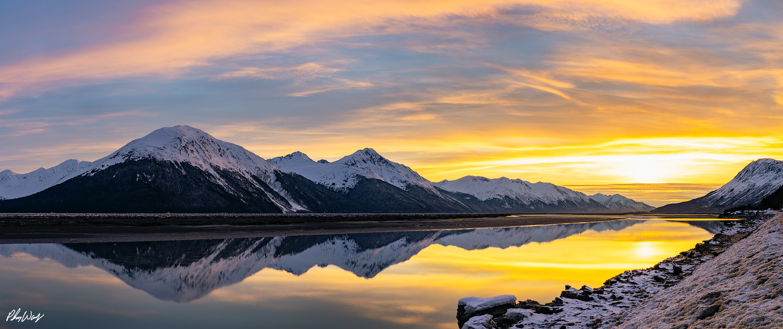 Alaska Dreaming Snow covered mountains reflected in calm water at sunset with golden clouds in Kenai Alaska.