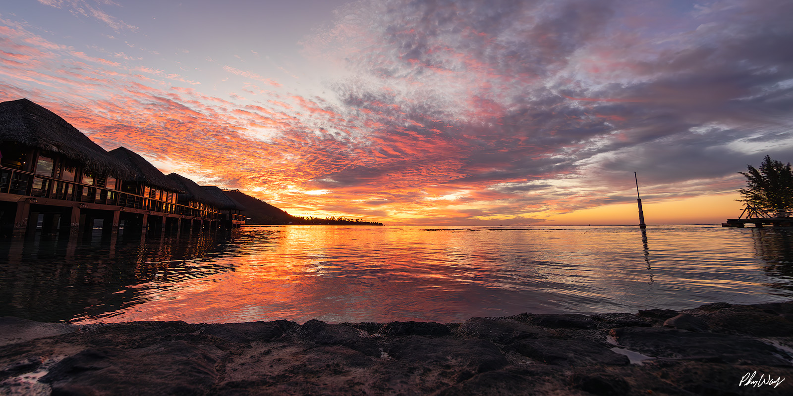 Mo'orea Paradise Sunset Colorful sunset reflecting over calm lagoon water with overwater bungalows in Mo'orea Tahiti.