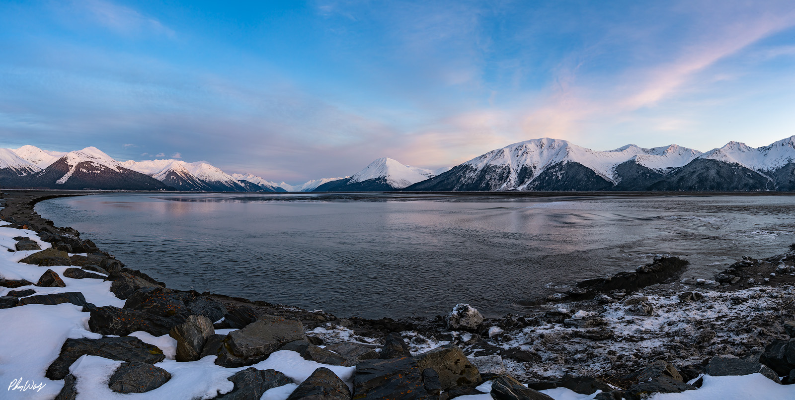 Cold Mountain Snow covered mountains and calm tidal water along a rocky shoreline in Kenai Alaska.