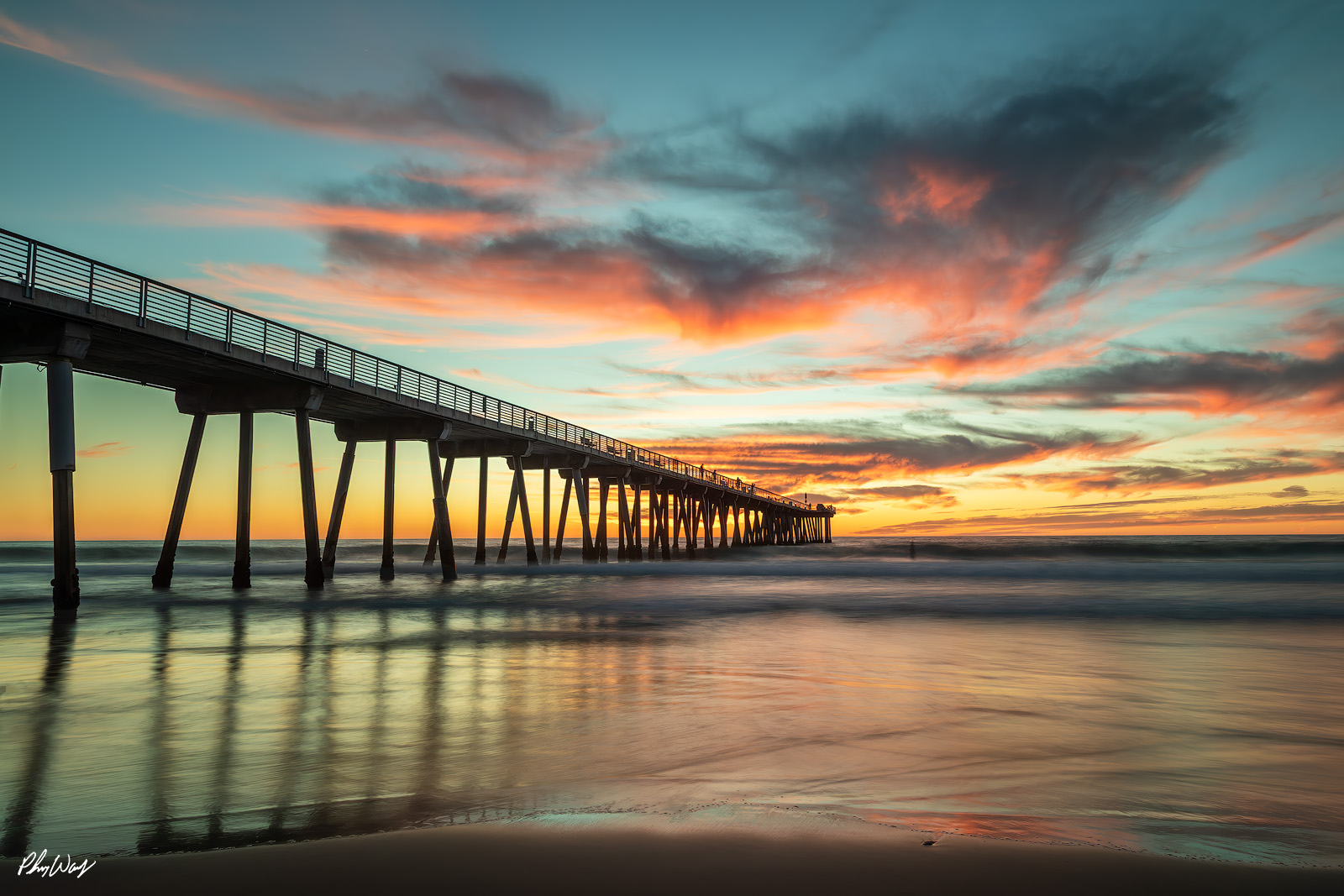 Pier View Sunset view of the Manhattan Beach Pier with colorful clouds and smooth ocean reflections in California.