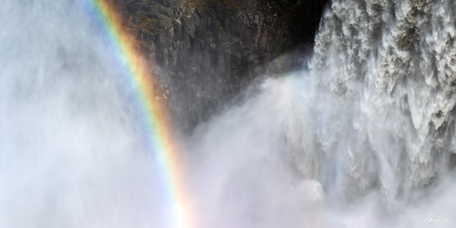 Beauty Carnage Rainbow cutting through mist beside powerful waterfall at Dettifoss Iceland.
