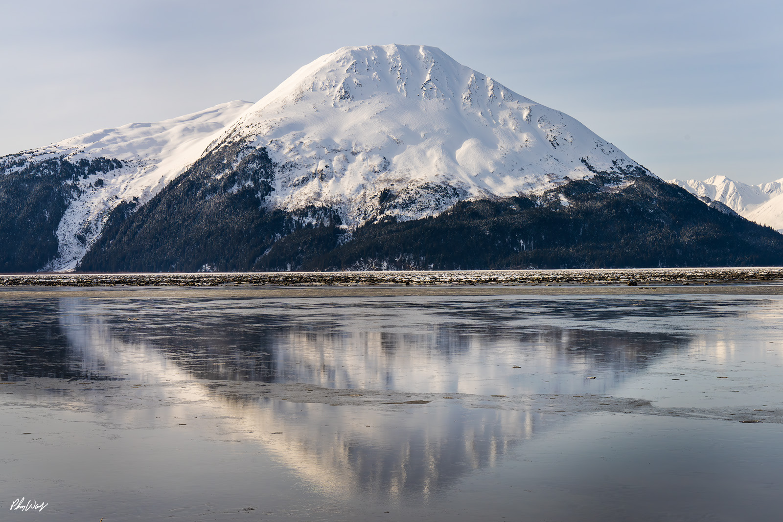 Reflecting Alaska Snow covered mountain reflected in calm icy water under a clear winter sky in Kenai Alaska.