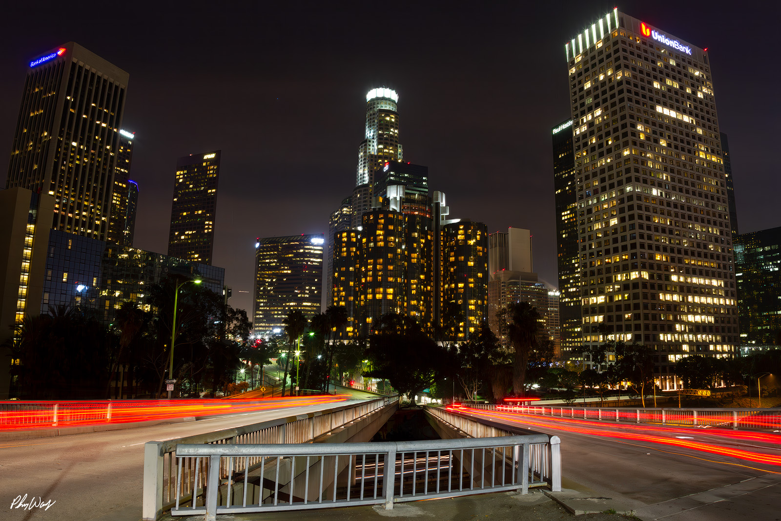 Downtown Los Angeles Lights Nighttime photograph of downtown Los Angeles skyline with long exposure red light trails crossing a bridge.