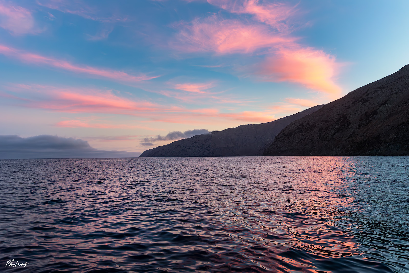 Guadalupe Sunset Soft pink and blue sunset reflecting on ocean water near Guadalupe Island Mexico with rugged cliffs in background.