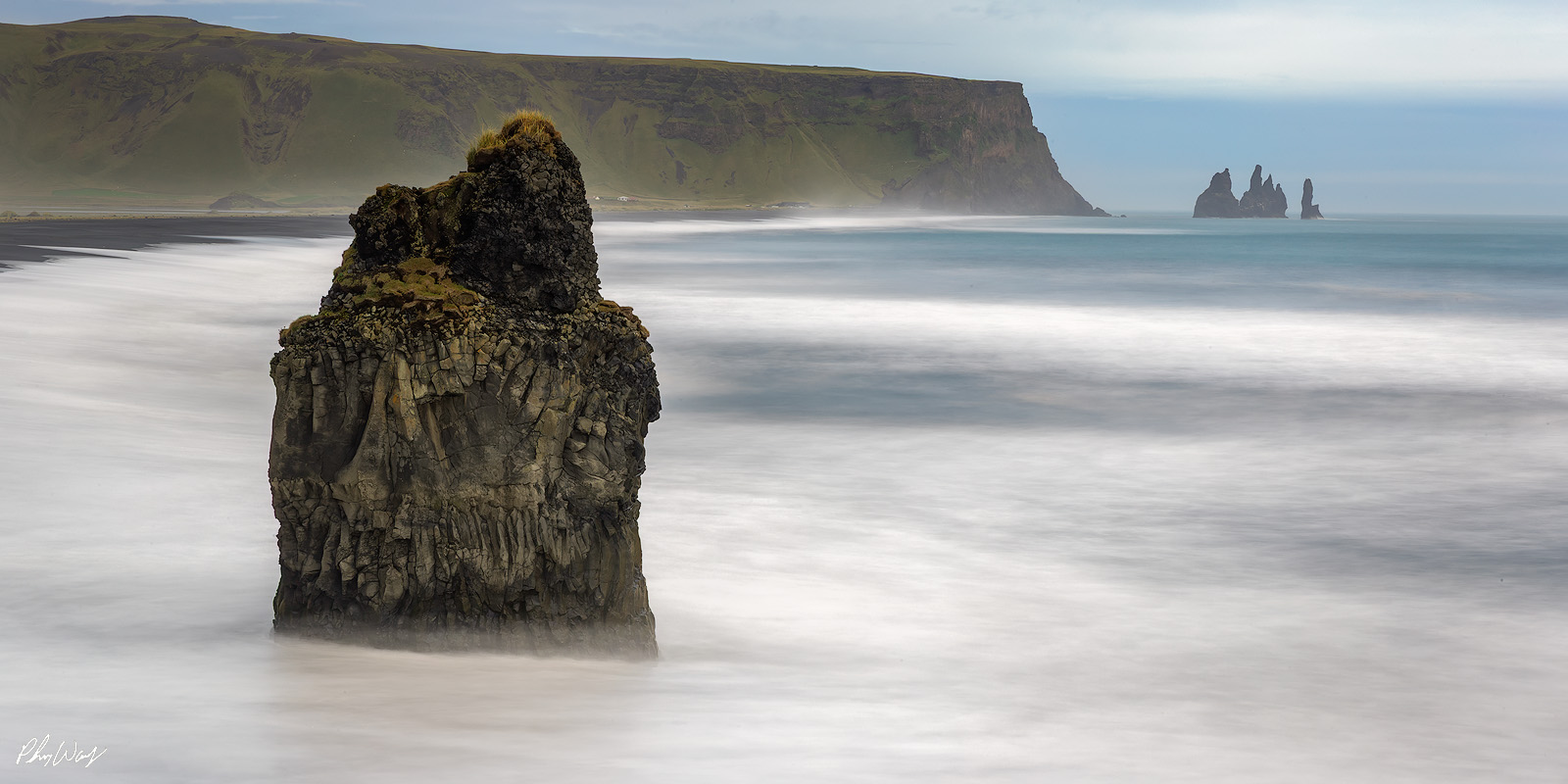 Coastal Iceland Sea stack rising from smooth ocean water at Reynisfjara Beach Iceland.