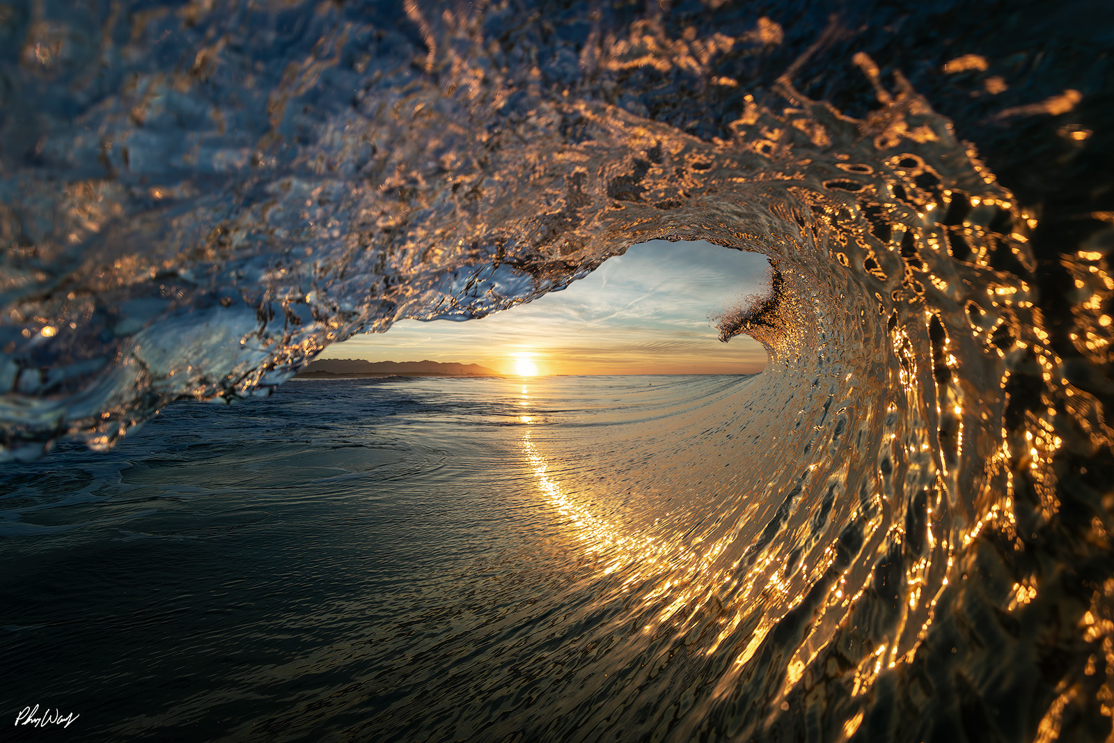 First Light Sun Trail Sunrise viewed through the interior of a curling ocean wave in Oxnard, Ventura County, California.