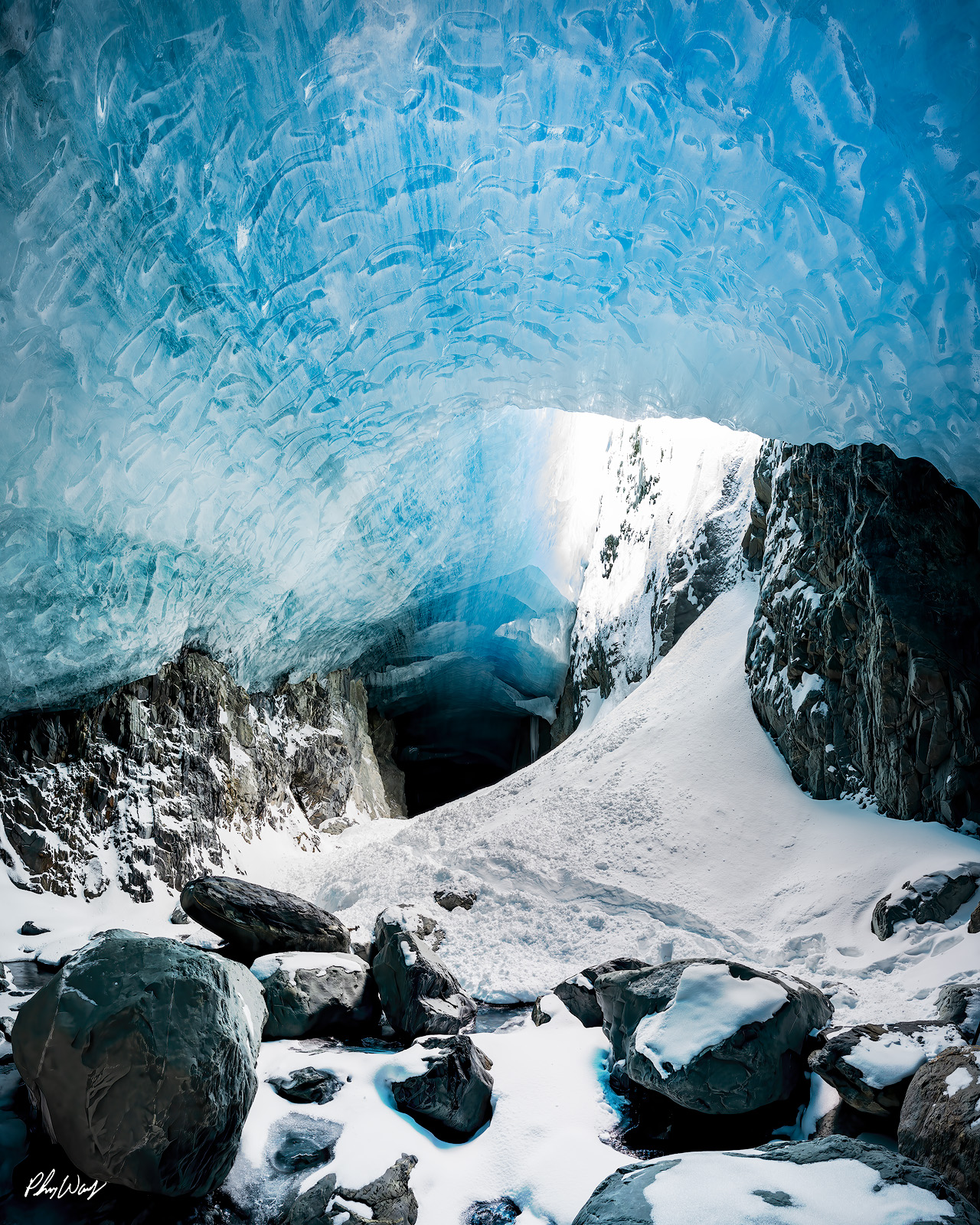 The Key Hole Blue glacier ice cave opening with snow covered rocks and light filtering through in Kenai Alaska.